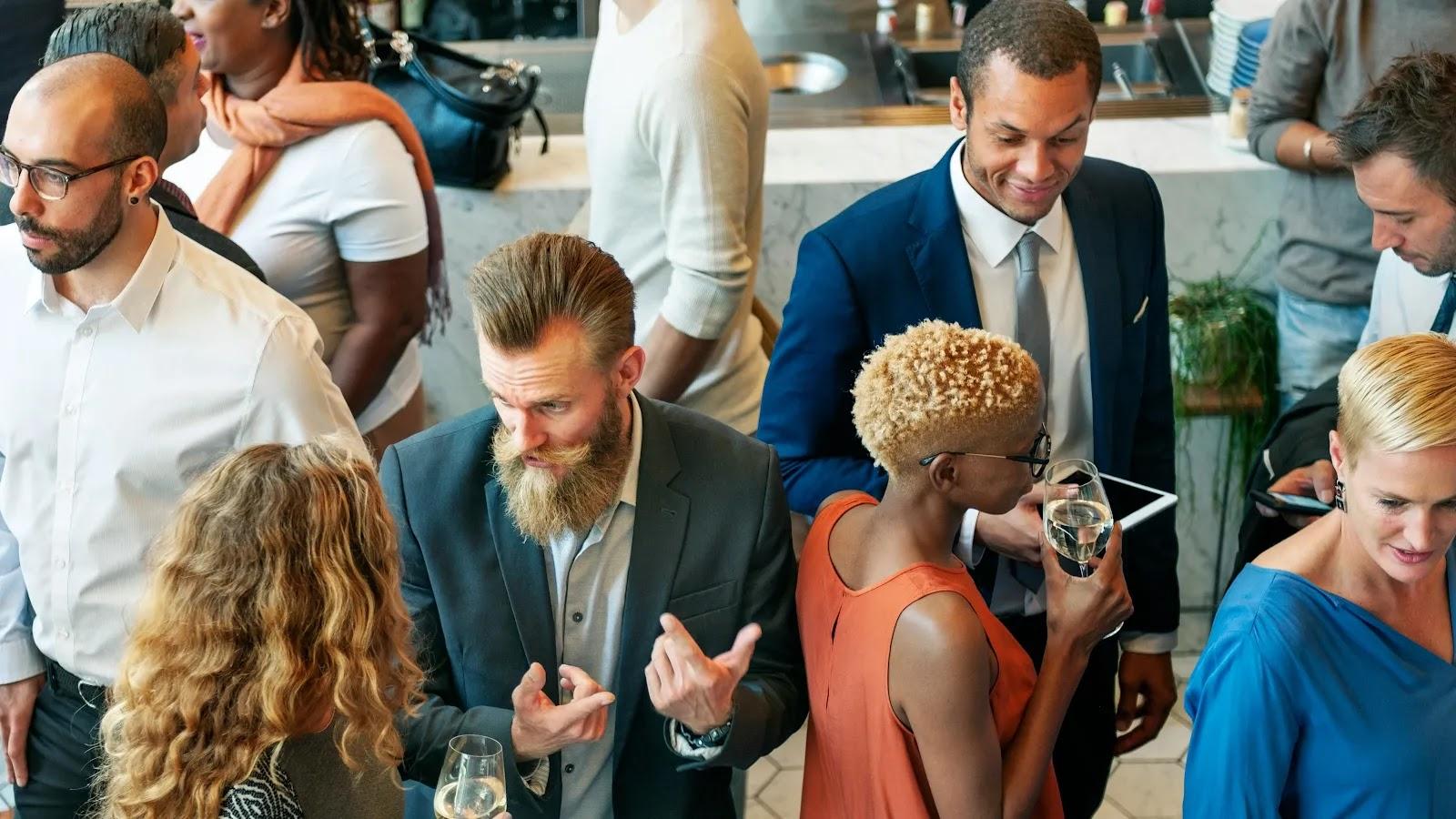About a dozen guests talking in small groups by a white marble counter, two of them holding glasses of white wine.