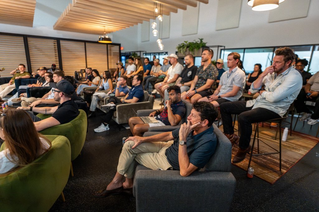 About twenty-five people seated in a lounge, listening to a speaker off frame