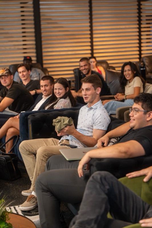 A row of attendees on a sofa smiling and laughing during a talk at an evening event
