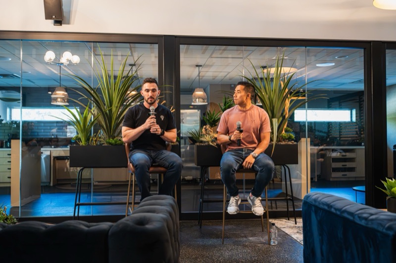 Full-length shot of a host in a black tee and jeans speaking into a microphone in a bright lounge