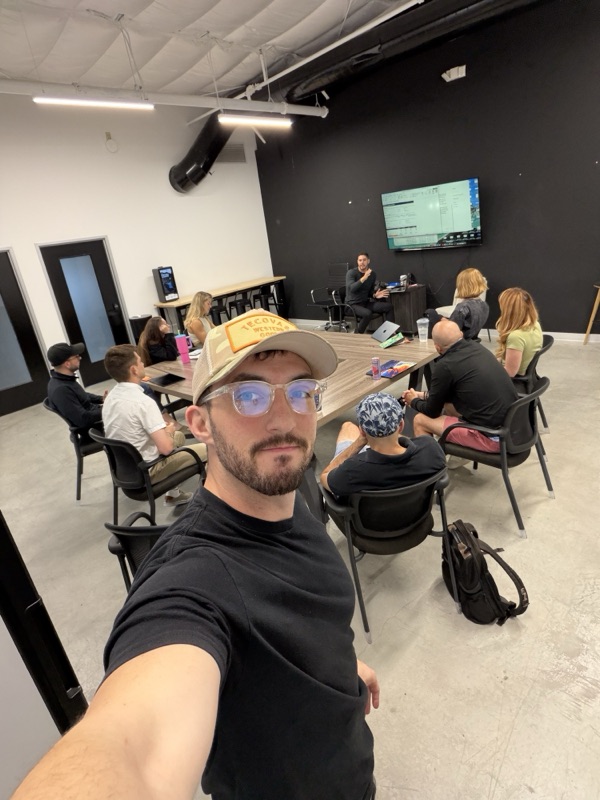 Attendee selfie in a workshop room with a presenter and group visible in the background